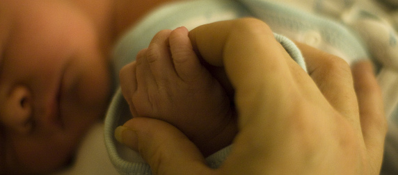 close-up of adult hand holding the hand of a sleeping newborn
