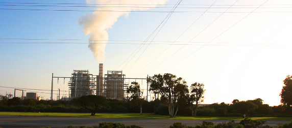 coal-fired power plant on the horizon, emitting smoke against a blue sky