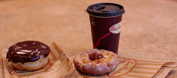 A Tim Hortons coffee cup with lid, next to a cake doughnut and a chocolate frosted filled doughnut