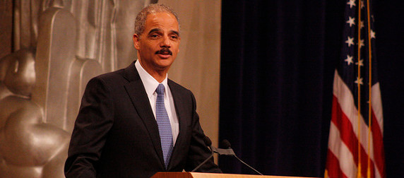 Eric Holder speaking at a podium, an American flag to his left