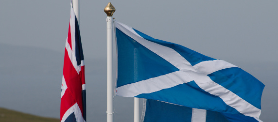 The Union Jack, hanging down, and the Scottish flag unfurled against an overcast sky