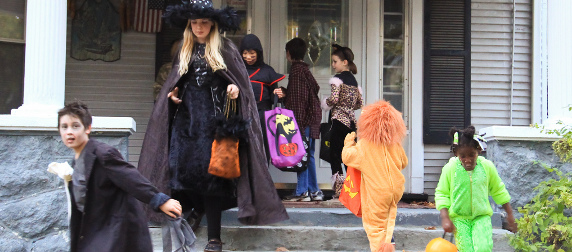 children in Halloween costumes approaching and leaving a front door to trick-or-treat