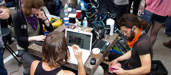 three Occupy Wall Street protestors work on laptops, one of them checking his phone