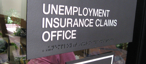 Black sign with white text that reads 'UNEMPLOYMENT INSURANCE CLAIMS OFFICE' with a braille translation beneath