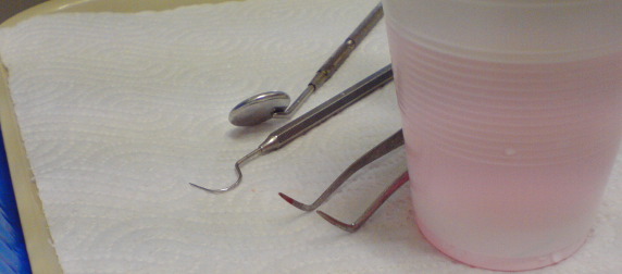 dentist's instruments and a cup of pink liquid arranged on a paper towel
