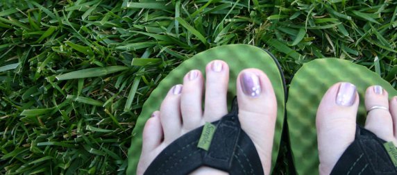 feet with painted toenails in flip-flops against a background of grass