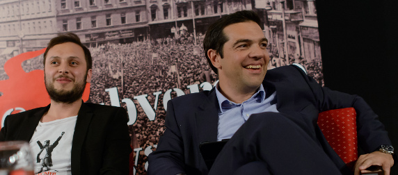 Alexis Tsipras and an unidentified man sitting in front of a banner at the Subversive Festival, Zagreb