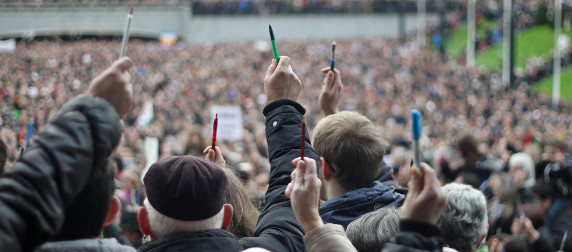 marchers, viewed from behind, holding up pens while facing a large crowd