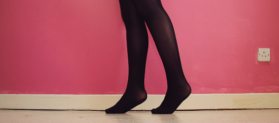 Person wearing black tights, shown from the knee down, against a red wall