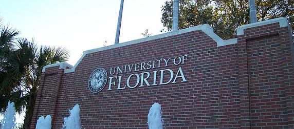 brick University of Florida sign with a fountain in the foreground, palm trees and sky in background