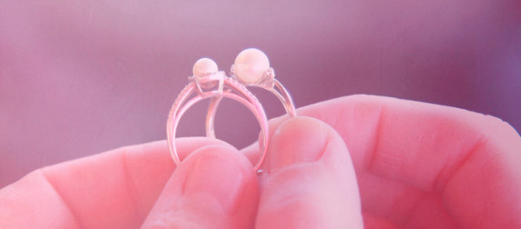 two pearl wedding rings, held against an abstract purple background