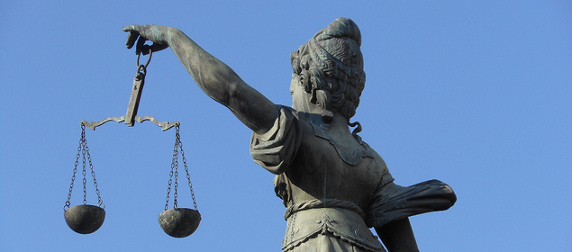 statute of Lady Justice holding scales, viewed from behind against a blue sky