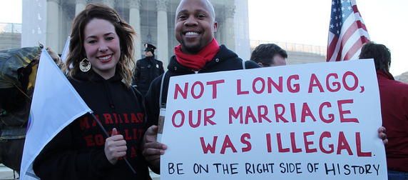 interracial couple holding a protest sign that reads, 'Not Long Ago, Our Marriage Was Illegal. Be On The Right Side Of History'