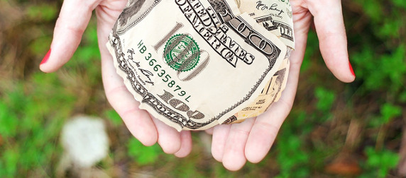 ball of U.S. dollars held in hands against an out-of-focus green and brown background