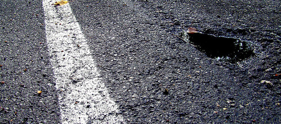 pothole in paved road, next to white traffic stripe