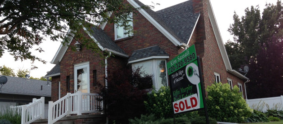 red brick house with SOLD realter sign in foreground