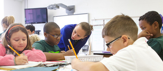 teacher working with elementary-aged students writing at a table