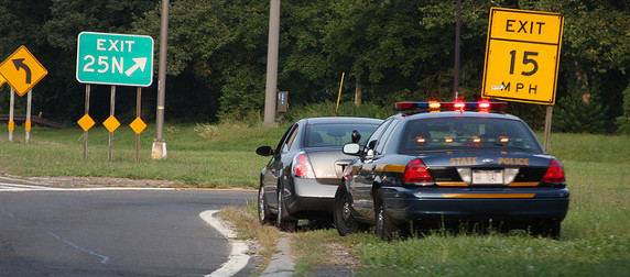 state police vehicle and civilian sedan pulled onto the shoulder near a highway exit