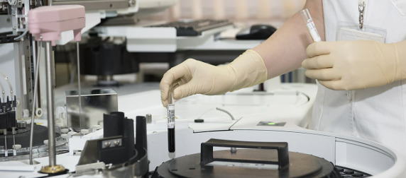 medical professional with gloves putting a vial of blood into a centrifuge