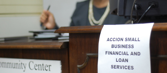 printed sign reading Accion Small Business Financial and Loan Services, taped to the edge of a desk