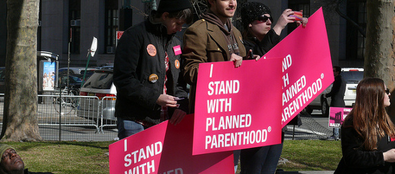 demonstrators hold pink signs that read I Stand With Planned Parenthood