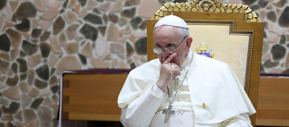 Pope Francis, seated and frowning, with a hand to his face