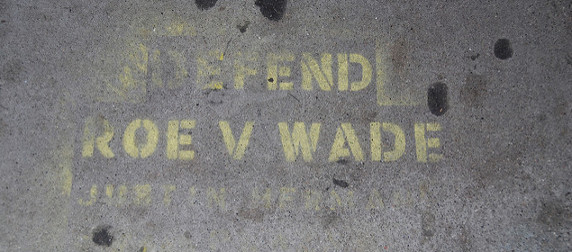 faded image, in yellow spray paint on concrete, reading DEFEND ROE V WADE