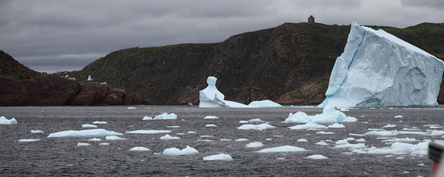 iceberg and loose ice spotted in the water, cliffs with a lighthouse in the background