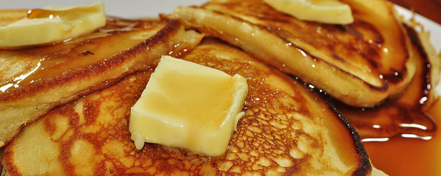 close-up of pancakes with pats of butter, drenched in maple syrup