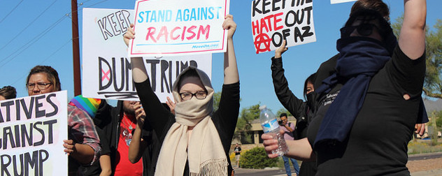 protesters holding signs that include 'Stand Against Racism' and 'Keep Hate Out of AZ'