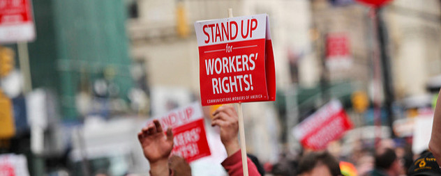 a protest sign that reads 'Stand Up for Workers' Rights! Communications Workers of America' held aloft over a crowd