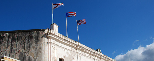 Cross of Bergundy, Puerto Rican and US flags flying over the Castillo de San Cristobal's facade