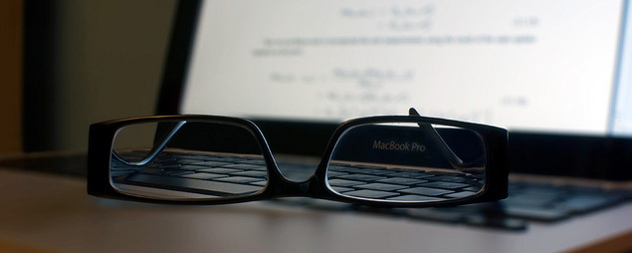 reading glasses resting on a MacBookPro keyboard, the screen illuminated but out of focus