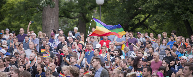 crowd gathered in a park, a rainbow flag held aloft in the center