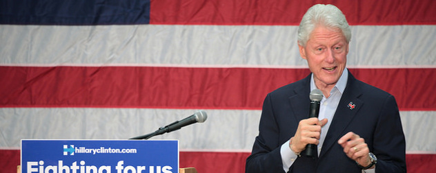 Bill Clinton speaking with a microphone in front of an American flag