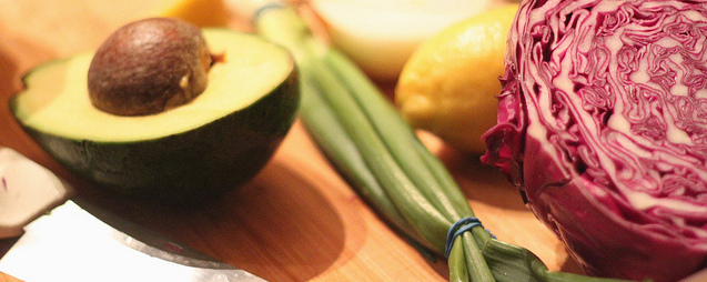 avocado, scallions, lemon and red cabbage with a knife on a cutting board