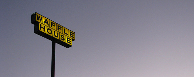 an illuminated Waffle House sign against a dawn sky