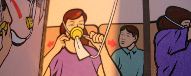 detail of an in-flight safety card showing an adult securing an oxygen mask with a child in the next seat