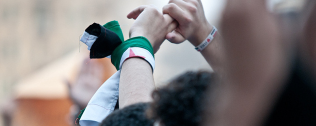 protester with raised hands wearing a Syrian flag around a wrist