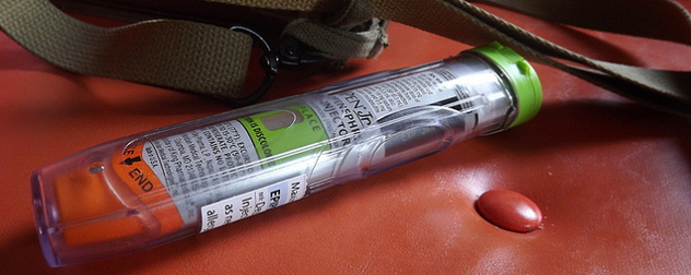 an EpiPen resting on a red leather seat next to a bag's strap