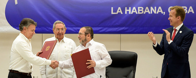 Juan Manuel Santos Calderon shakes the hand of Timoleon Jimenez while Raul Castro looks on and an observer claps