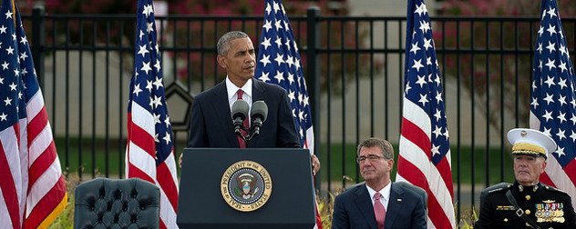 President Obama speaking at an outdoor podium in front of a row of American flags, 