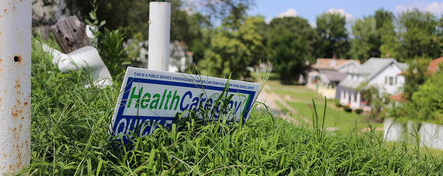 yard sign advertising HealthCare.gov, obscured by tall grass