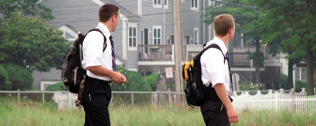 two young men in short-sleeve shirts and ties, with backpacks, turned away from the camera