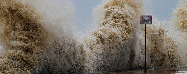 surging ocean behind a small sign that reads Caution Drop Off