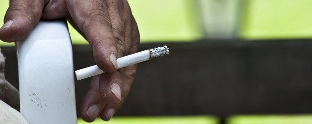 hand leaning on a railing, holding a lit cigarette