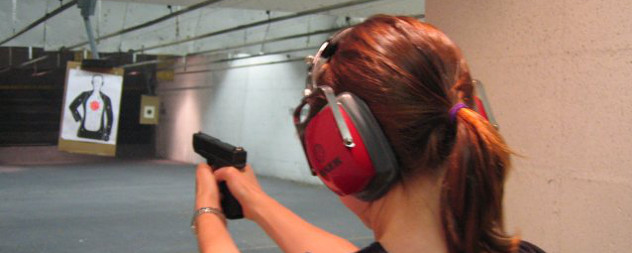 person with a ponytail, viewed from behind, firing a Glock 23 at a gun range