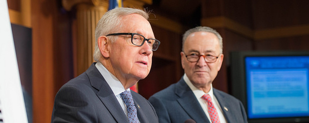 Harry Reid speaks at a podium while Chuck Schumer looks on