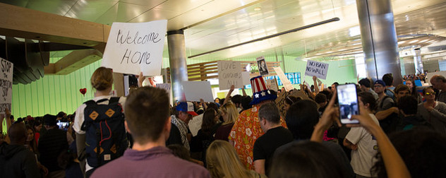 Protesters against Trump's executive order on immigration hold signs that read 'Welcome Home,' 'No Ban, No Wall,' and 'Love Conquers All'