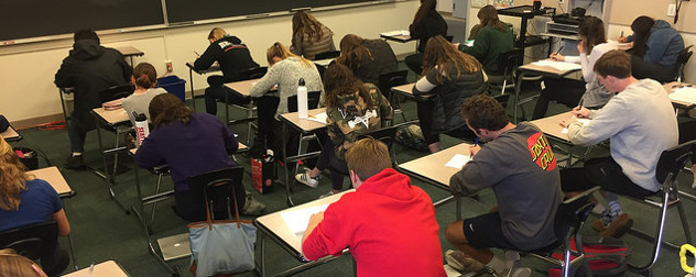 students seated at desks, working on exams, seen from behind